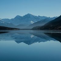 Snow-capped mountains reflected in a calm alpine lake Mountain lake reflecting snow-capped peaks under blue sky